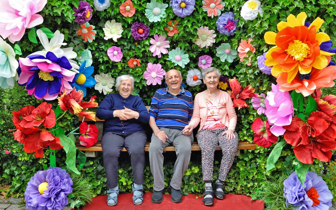 Zwei Seniorinnen und ein Senior sitzen auf einer Bank und strahlen.